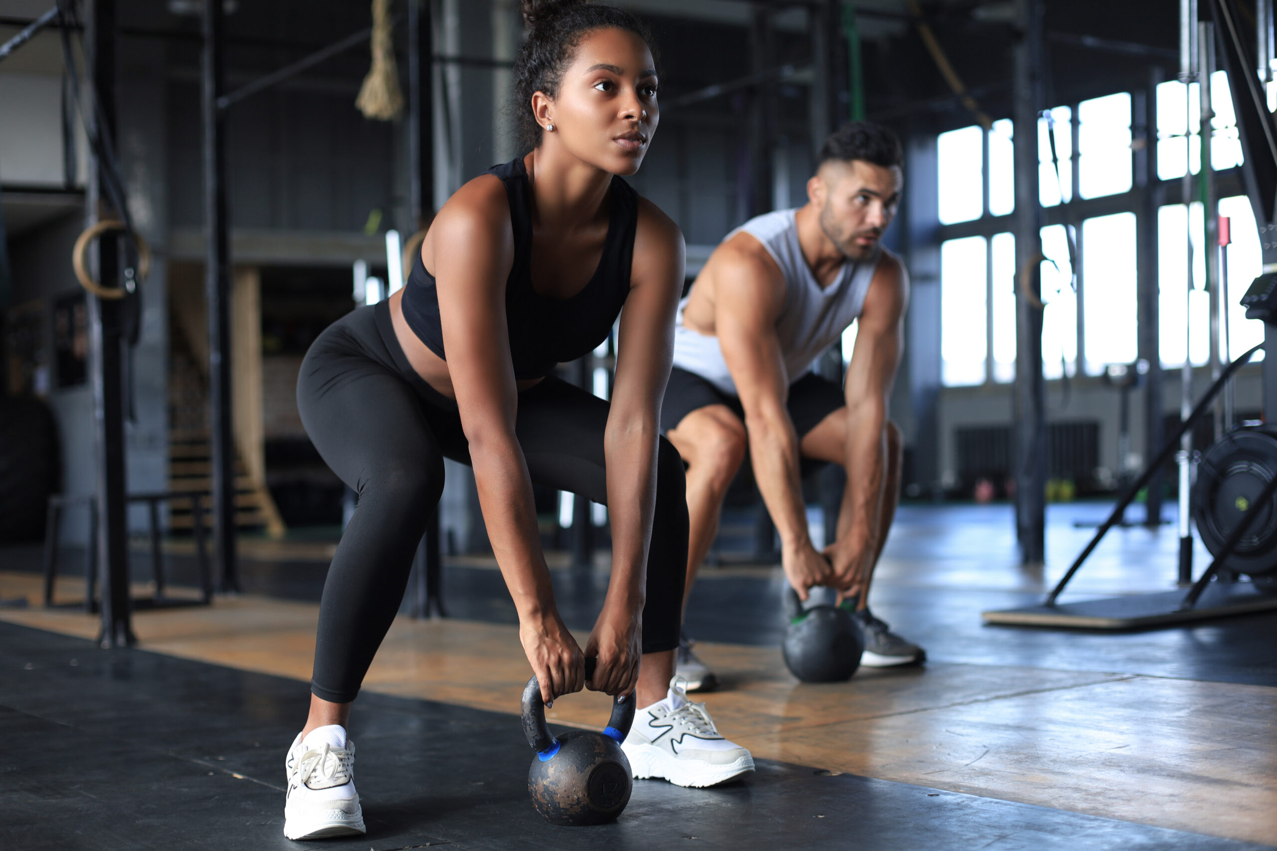 fit and muscular couple focused on lifting a dumbbell during an exercise class in a gym.
